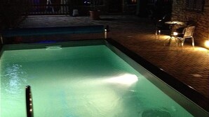 A swimming pool with a clear edge, surrounded by a stone-tiled deck and outdoor seating.