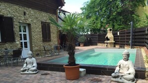 A courtyard with a swimming pool, two Buddha statues, a stone building, and outdoor furniture.