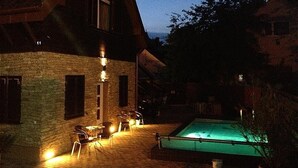 A stone building with a swimming pool and outdoor seating area at night.