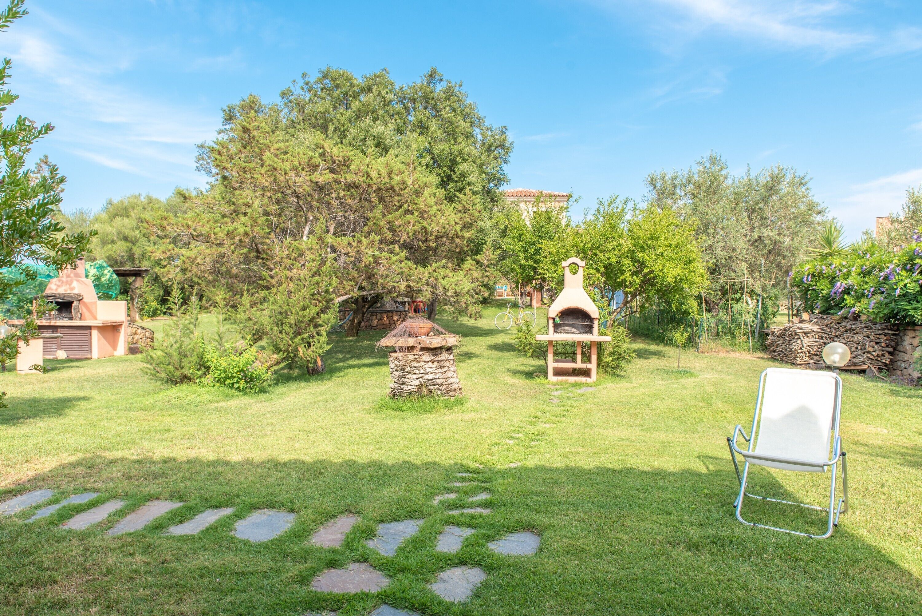 Un jardín con un banco de piedra, un comedero para pájaros y una parrilla.
