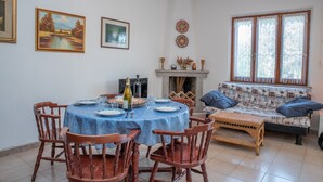 Un comedor con una mesa redonda, sillas y mantel azul. Hay un sofá con cojines y una ventana con cortinas.