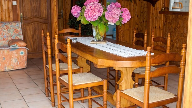 A wooden dining table with six chairs, a vase with pink flowers, and a wooden cabinet in the background. - Homerez - House in Orsanco (Orsanco)