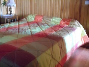 Un lit recouvert d’une courtepointe aux couleurs vives, dans une pièce aux murs en bois.