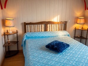 A bedroom with a wooden headboard, two bedside lamps, a patterned bedspread, and a blue pillow. - Homerez - House in Orsanco (Orsanco)