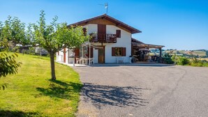 A two-story house with a covered porch, a gravel driveway, and a grassy area with trees. - Homerez - House in Orsanco (Orsanco)