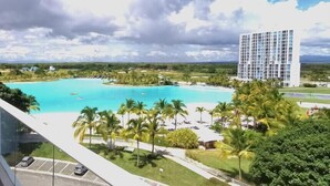 A resort with a large pool, palm trees, and a tall hotel building. - Apartamento en Playa Blanca Town Center (Rio Hato)