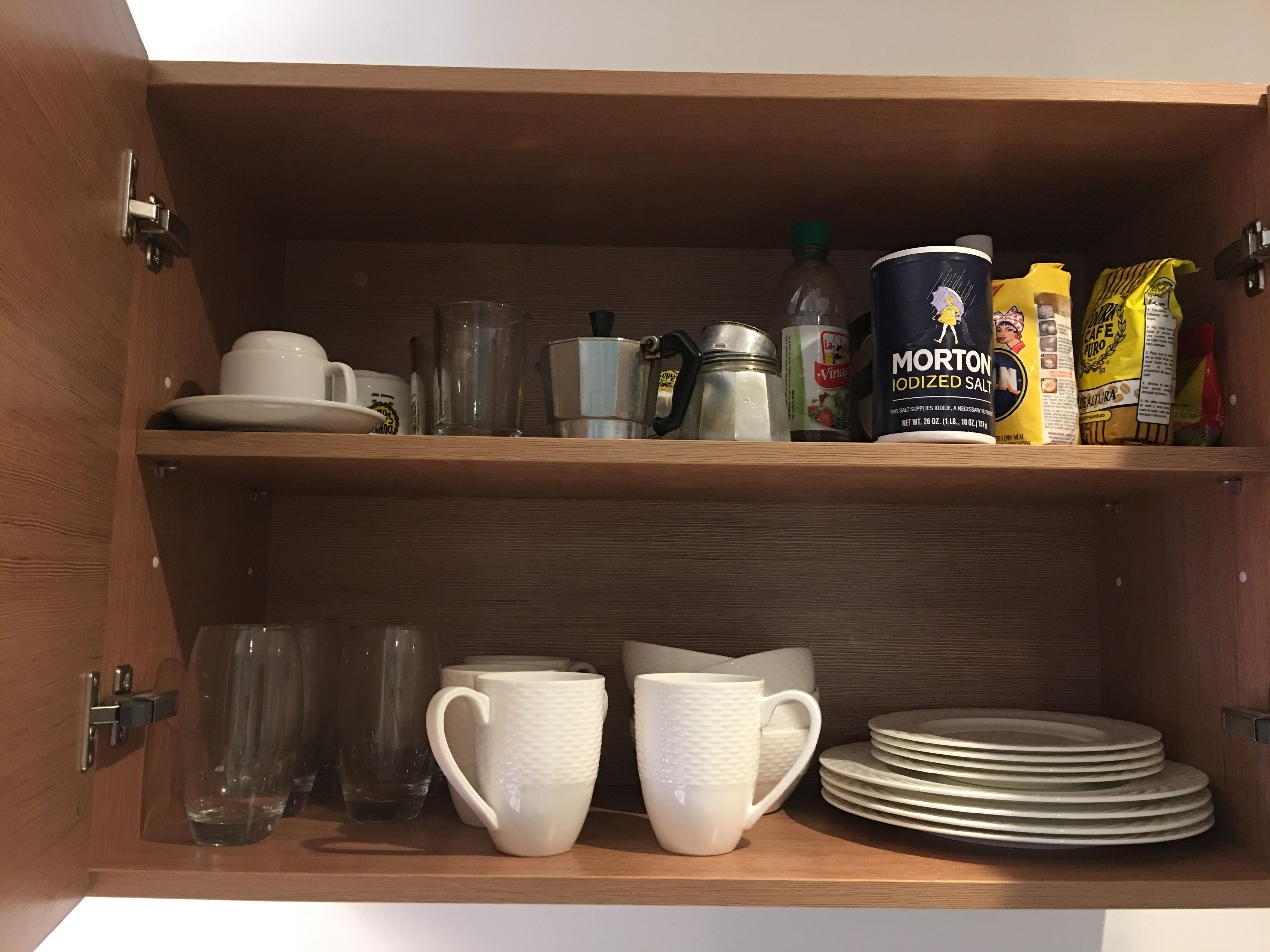 A wooden cabinet with kitchenware including cups, plates, a coffee pot, and salt containers.