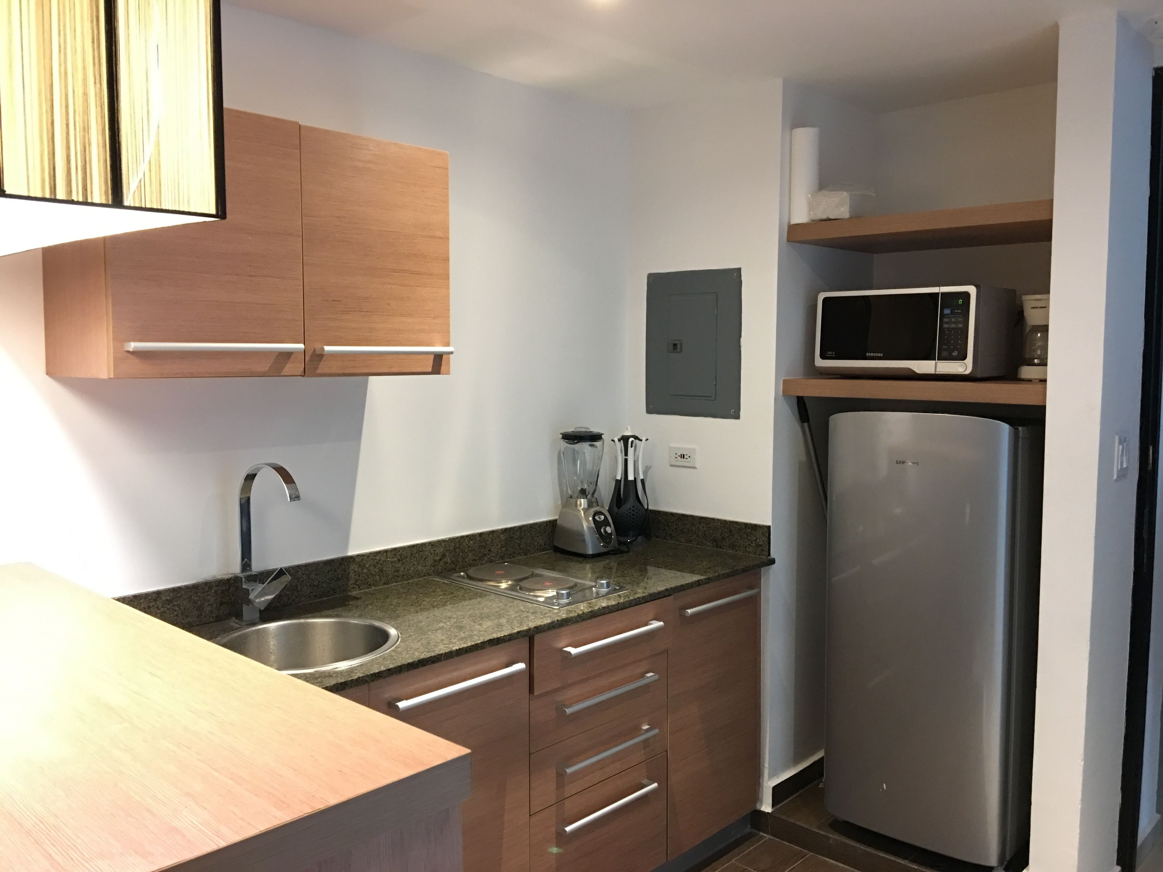 Una cocina moderna con armarios de madera, un lavamanos de acero inoxidable, microondas integrado y refrigerador.