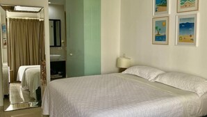 A hotel room with a large bed, a mirror, a door leading to a bathroom, and a wall with framed pictures. - Apartamento en Playa Blanca Town Center (Rio Hato)