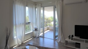 Una sala de estar moderna con televisor de pantalla plana, una mesita y vista a un balcón.