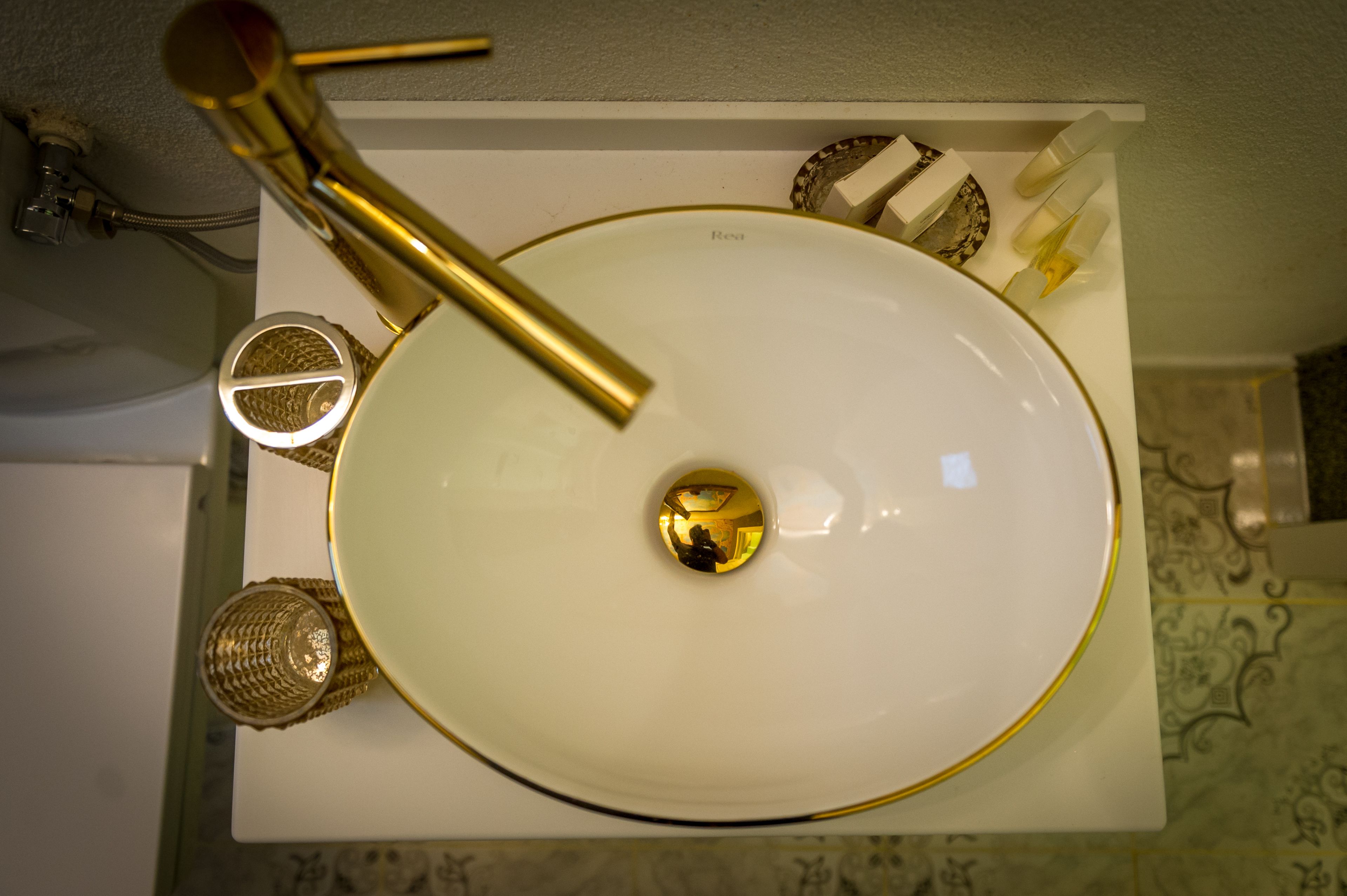 A bathroom sink with a gold faucet, a gold-rimmed mirror, and a gold-rimmed bowl.