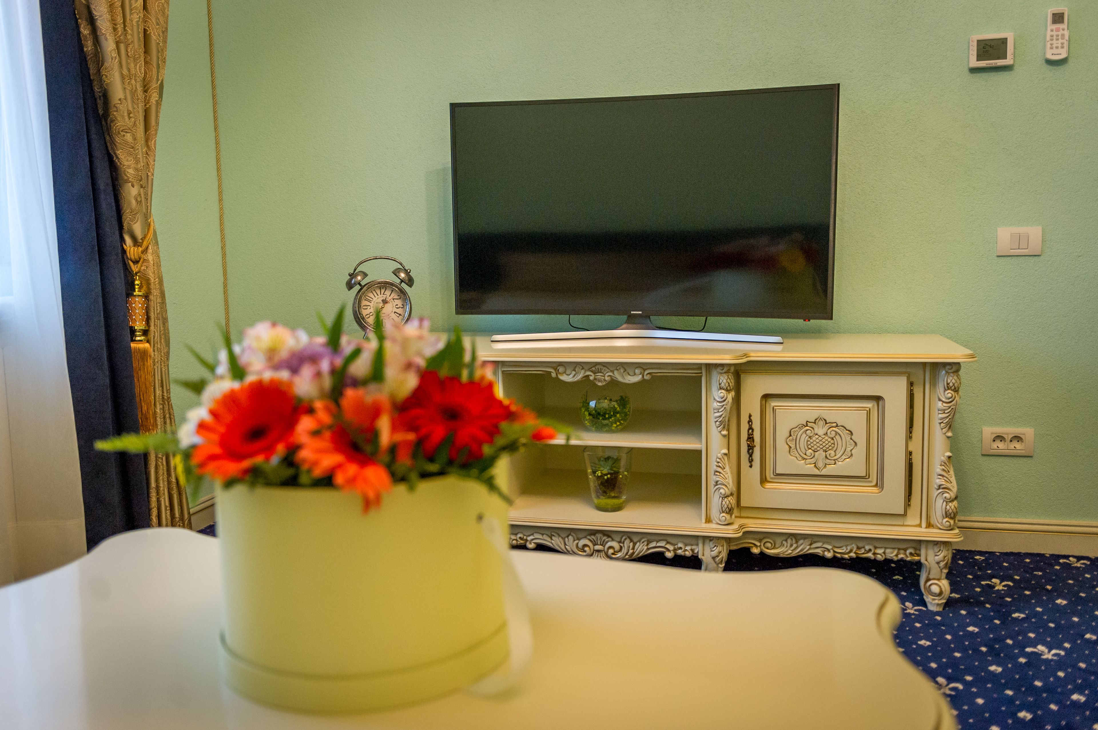A hotel room with a television on a stand, a small cabinet, and a vase of flowers on the table.