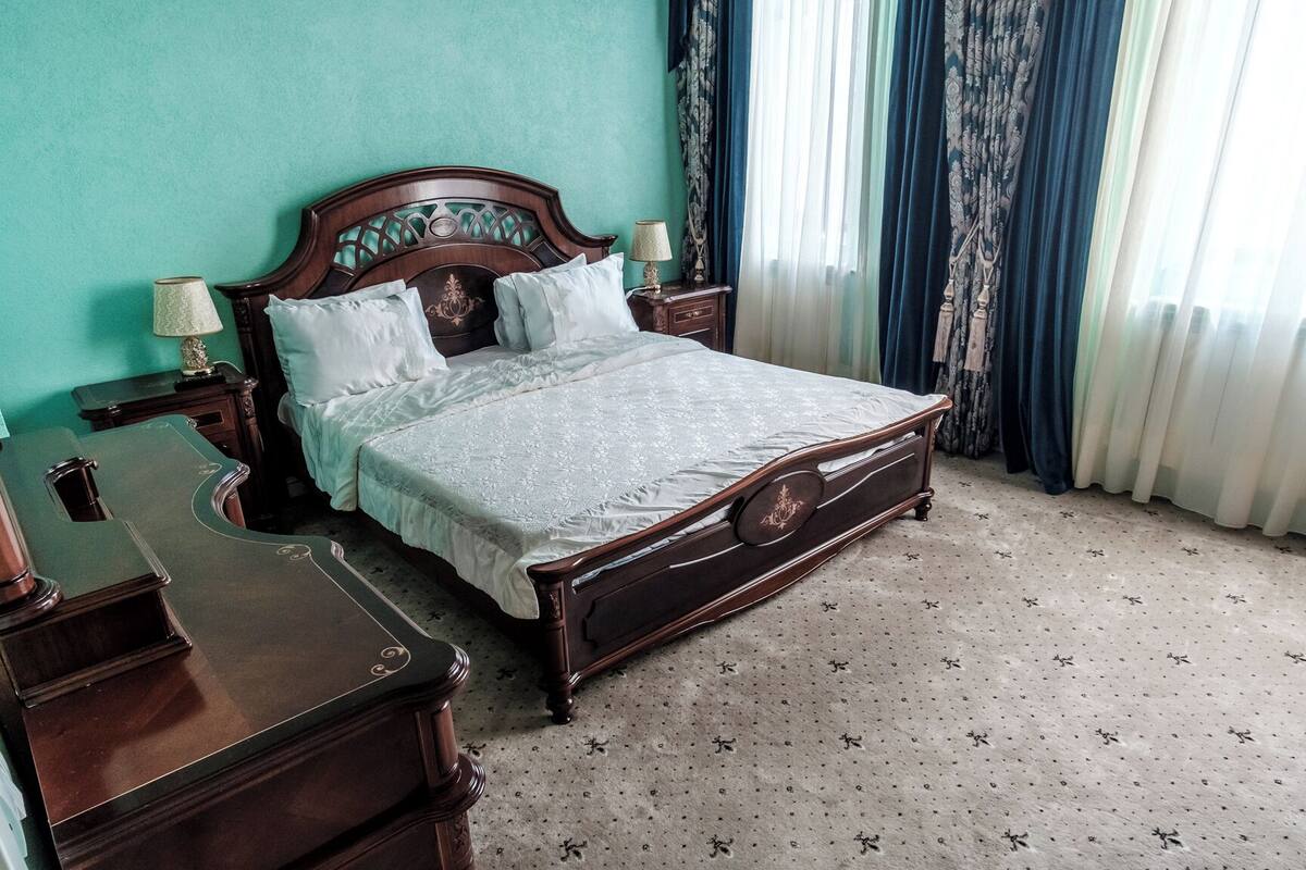 Un lit à baldaquin classique, doté d’une structure en bois et d’une couvre-lit à motifs floraux, placé contre un mur de couleur turquoise.