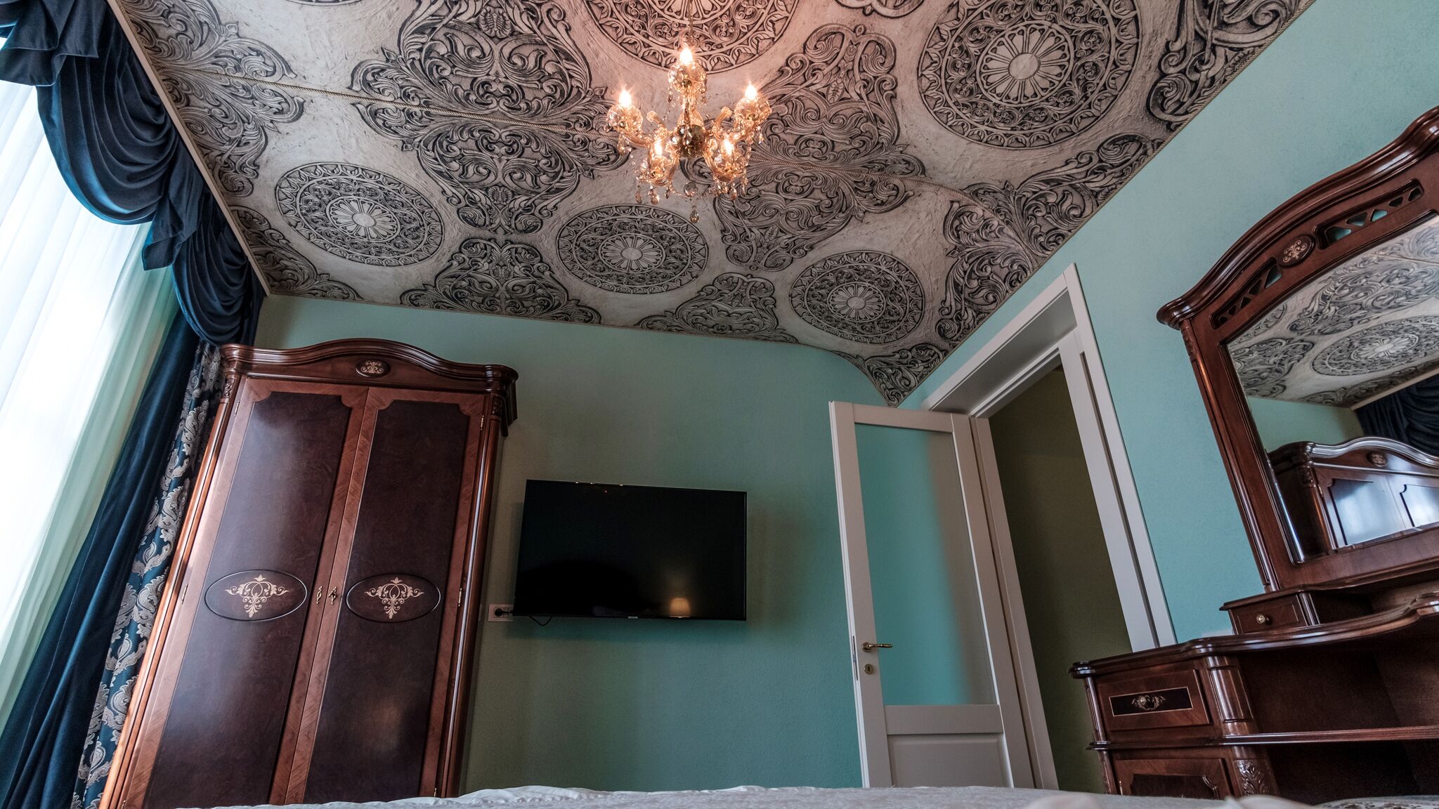 A bedroom with a large bed, a wardrobe, a dresser, and a television on the wall.
