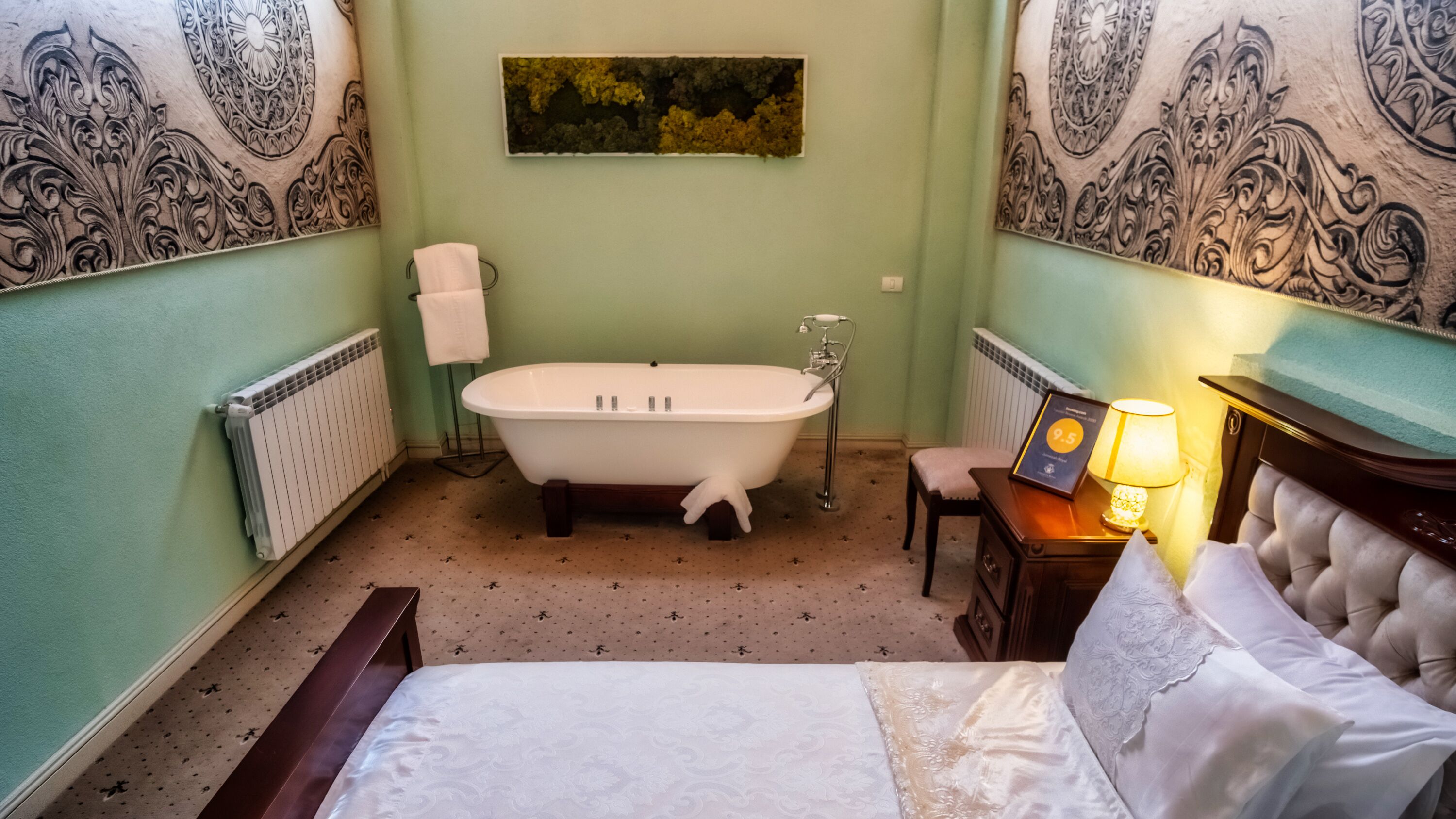 A room with a large bed, a bathtub, a small table with a lamp, and a chair.