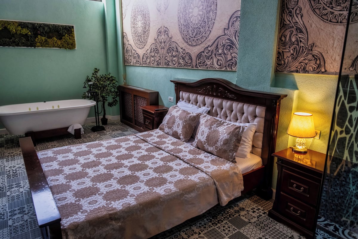 Une chambre à coucher comprenant un lit, une table de chevet, une lampe, un miroir fixé au mur et une baignoire.