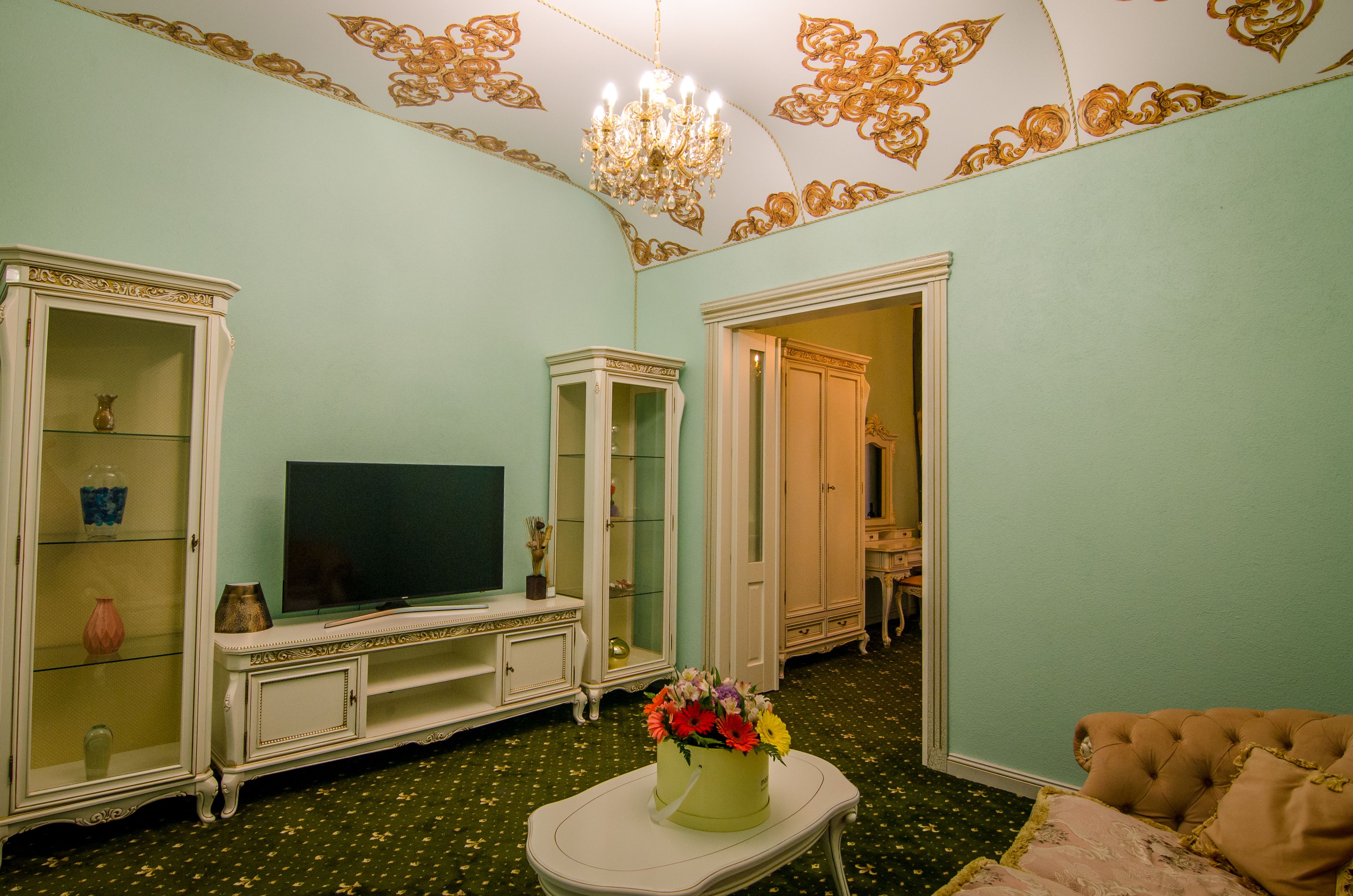 A living room with a television, a floral arrangement, and a chandelier.