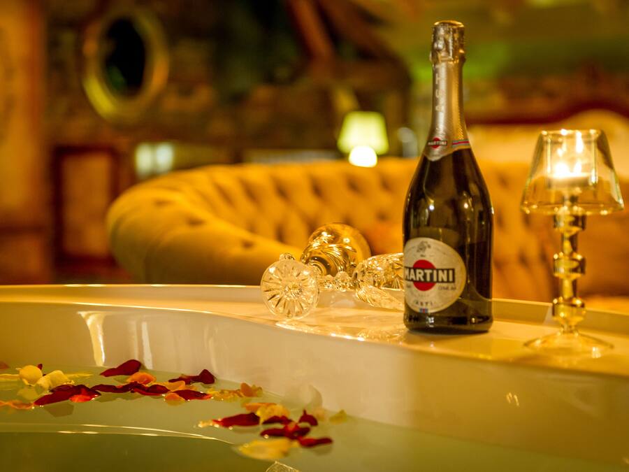 Una botella de vino Martini, una copa y cristalería decorativa sobre una mesa con pétalos de rosa.