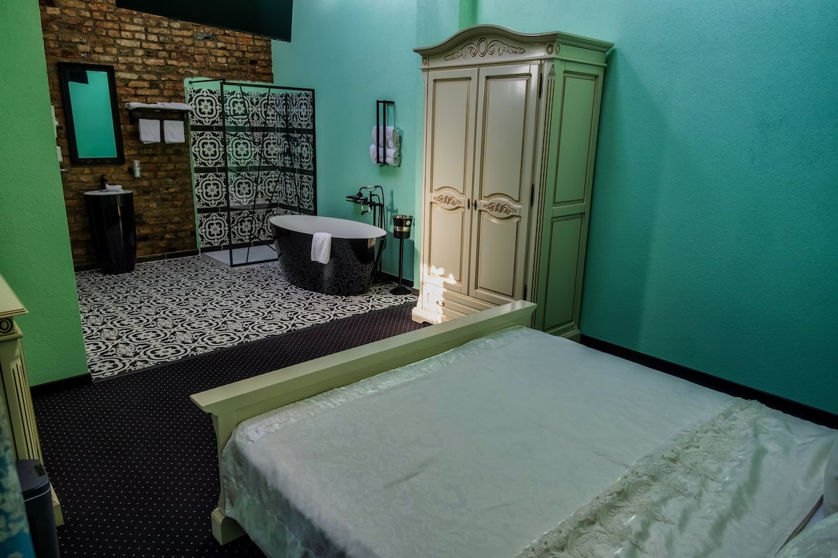 Une chambre d’hôtel avec un lit, une petite table, une armoire et une salle de bain avec une douche décorée.