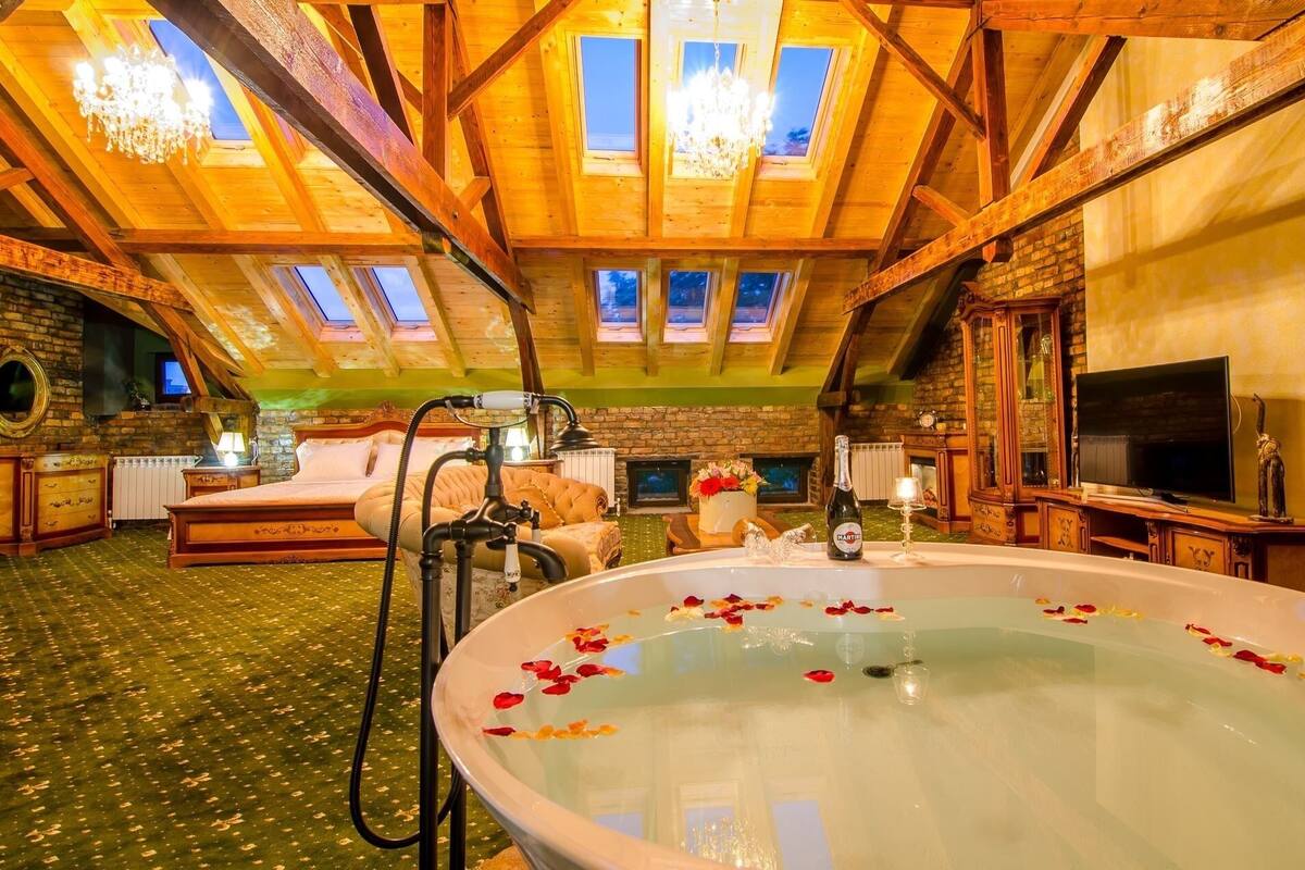 Une chambre confortable située dans les combles, avec une grande baignoire, des poutres apparentes, une cheminée et un téléviseur.