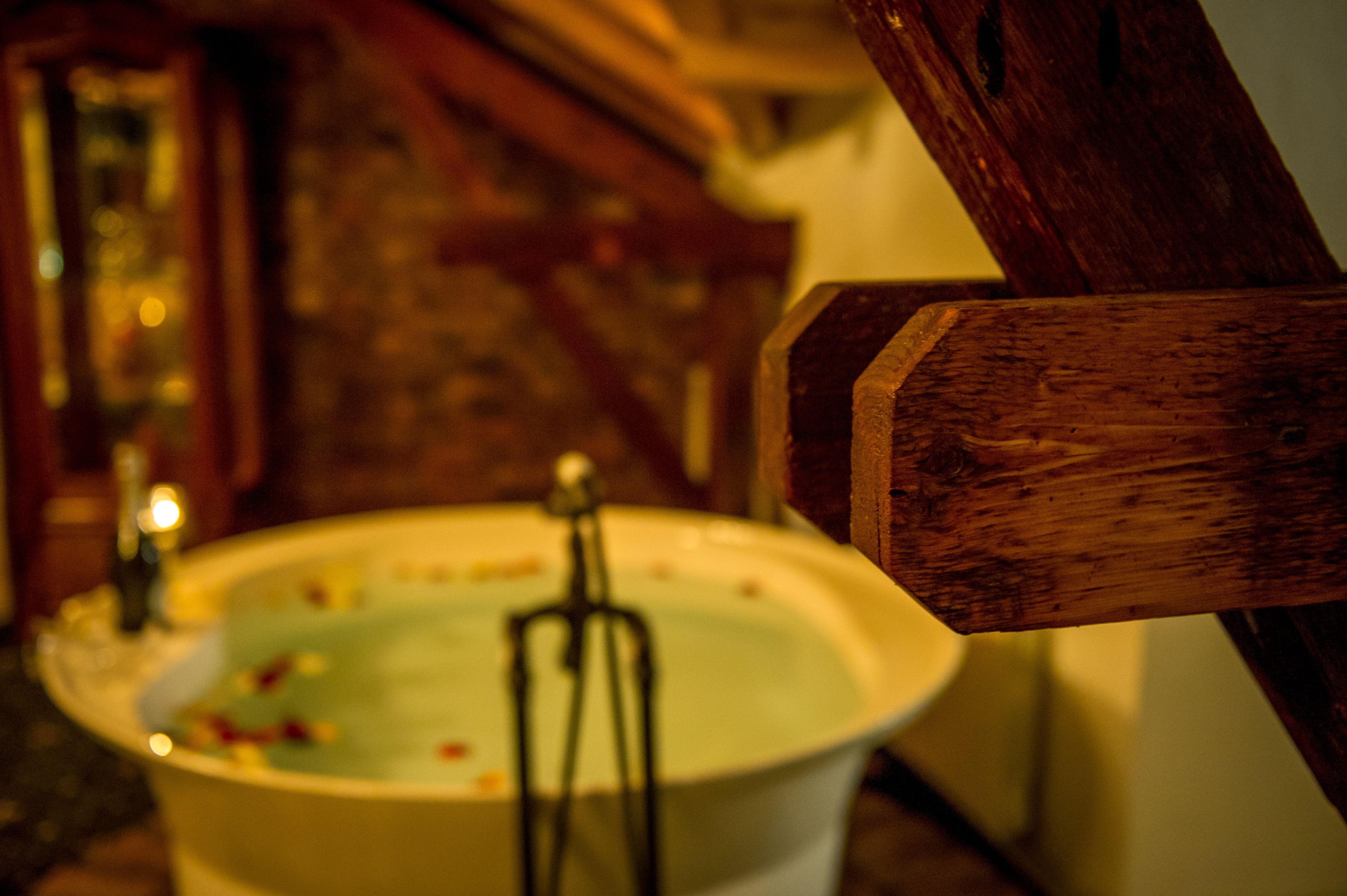 A bathtub with a wooden frame, a stone wall in the background, and a small window.