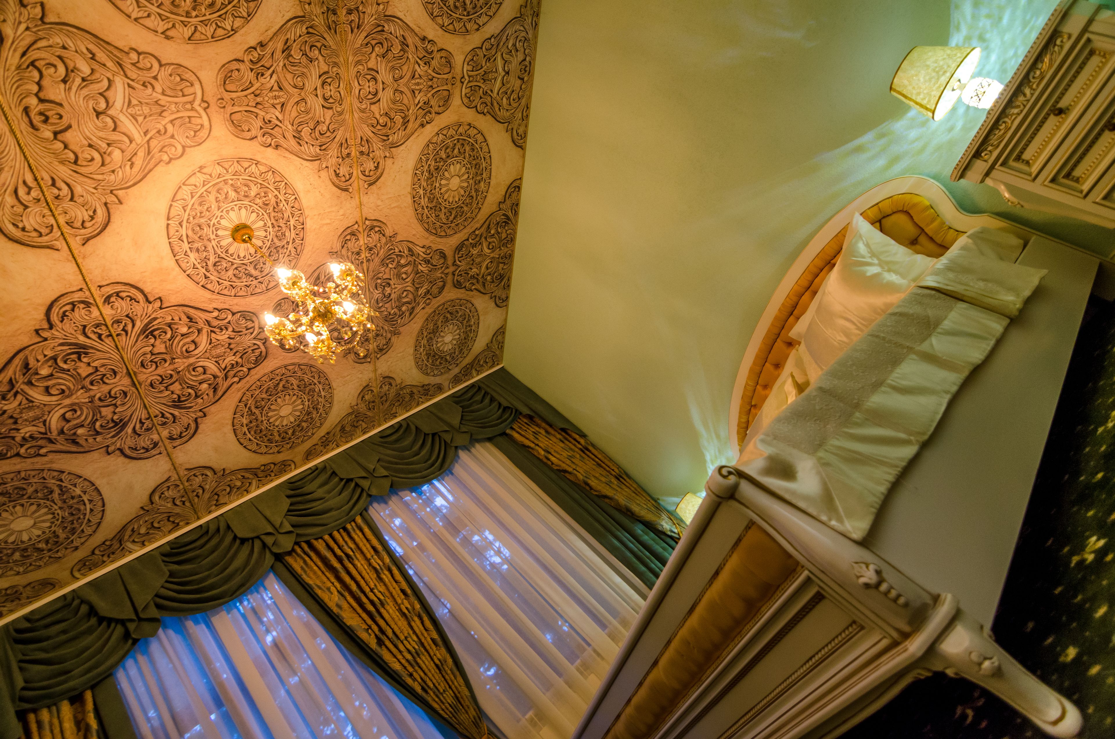 A room with ornate ceiling patterns, a bed with white linens, and a classic telephone.