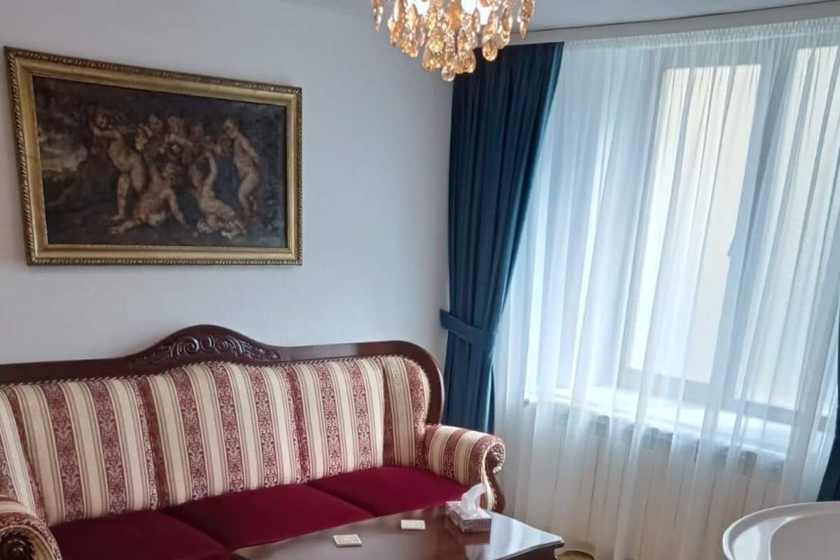 Un salon avec un canapé à rayures, une table basse en bois, un tableau accroché au mur et une fenêtre avec des rideaux.