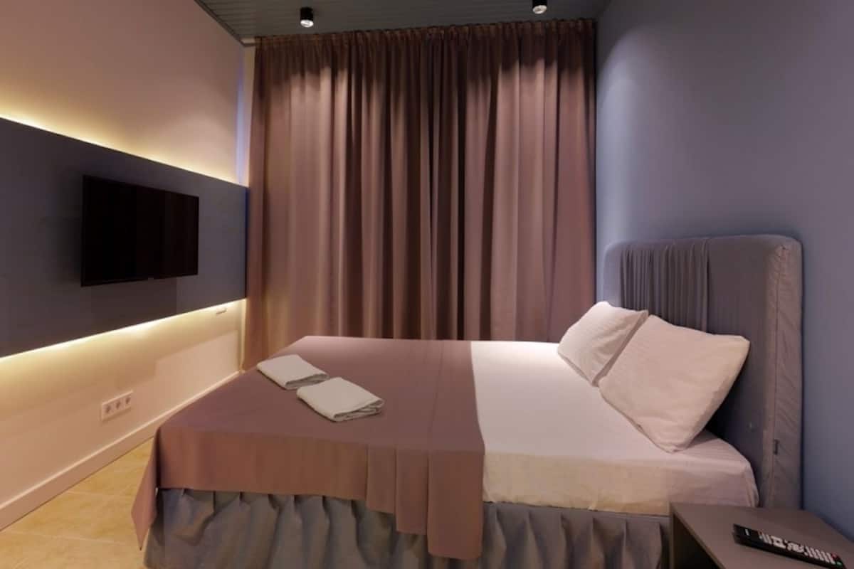 A modern bedroom with a bed, a flat-screen TV mounted on the wall, and a bedside table with a remote control.