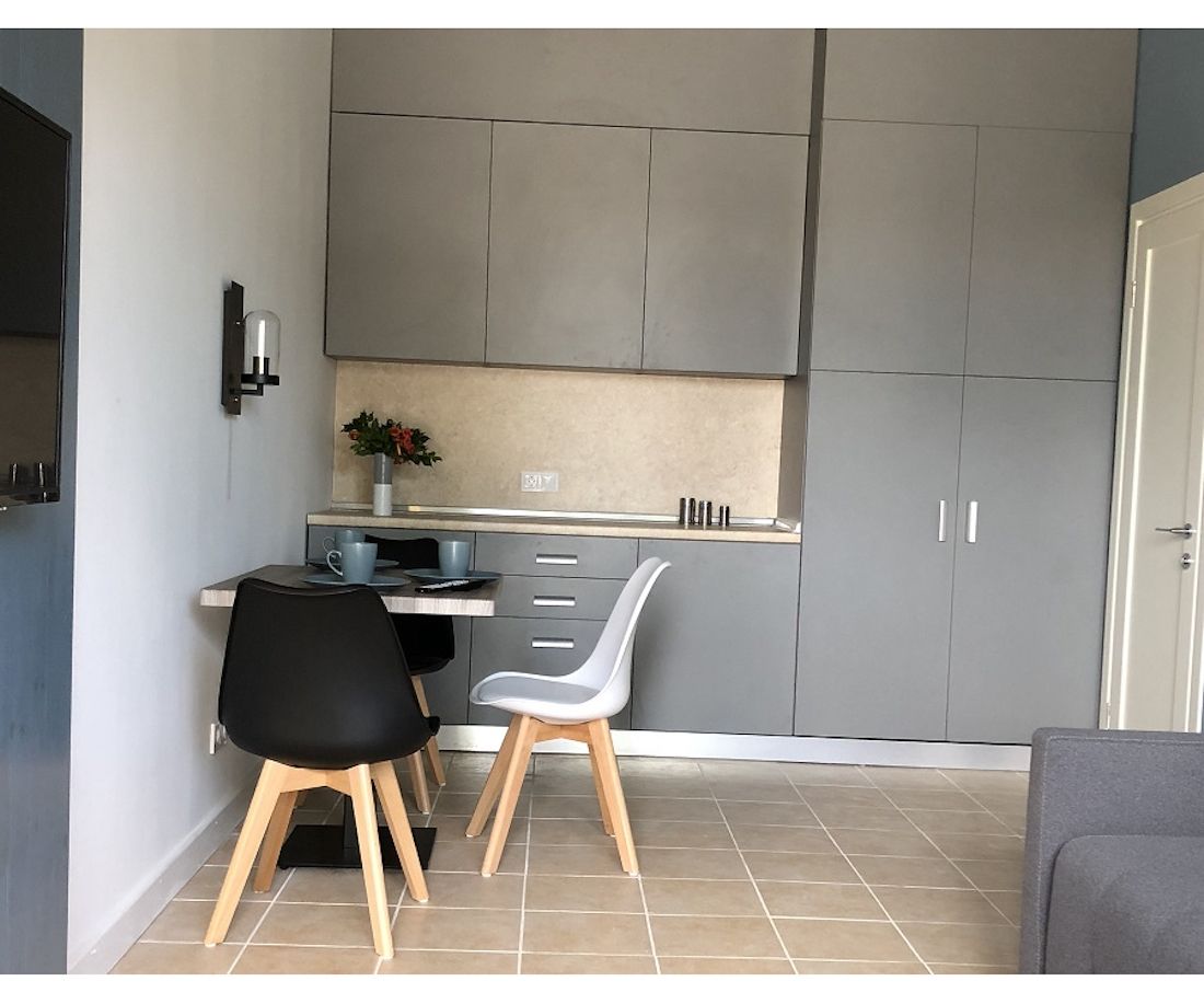 A compact kitchen with grey cabinets, a small dining table, two chairs, and a coffee machine.