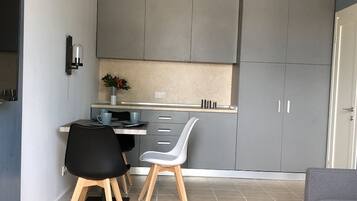 A compact kitchen with grey cabinets, a small dining table, two chairs, and a coffee machine.