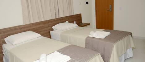 Ein Hotelzimmer mit zwei Einzelbetten, jeweils mit einem Holzkopfstück, weißen Kissen und ordentlich gefalteten Handtüchern.