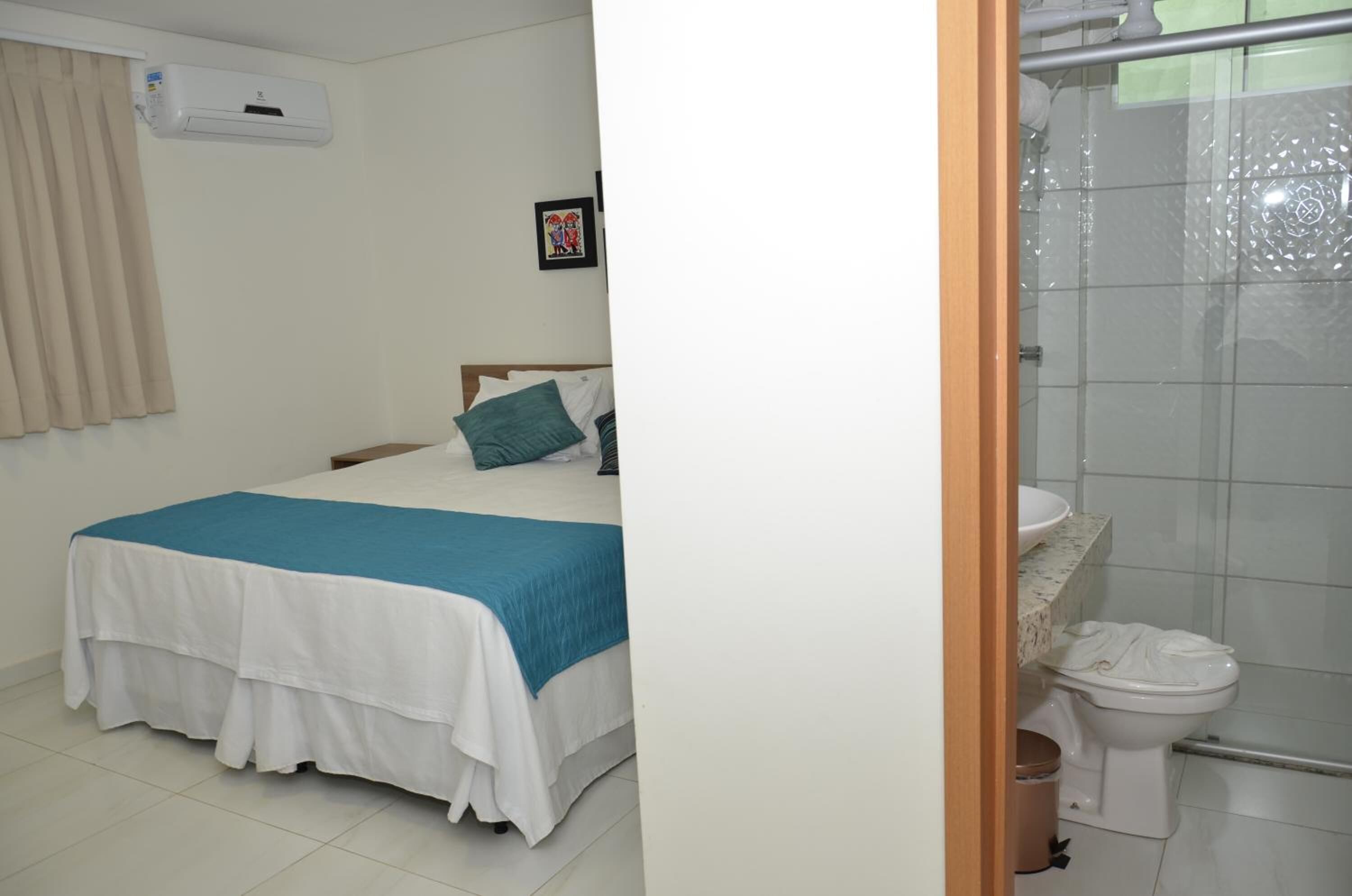 Un dormitorio con cama, mesita de noche, aire acondicionado de pared y un cuadro enmarcado.