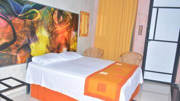 A hotel room with a bed, a large abstract painting on the wall, a yellow curtain, and a door.