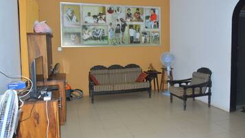 Una sala de estar con sofá, sillón, ventilador, televisor y un collage en la pared.