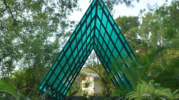 A structure with a geometric design, surrounded by greenery and steps leading up to it.