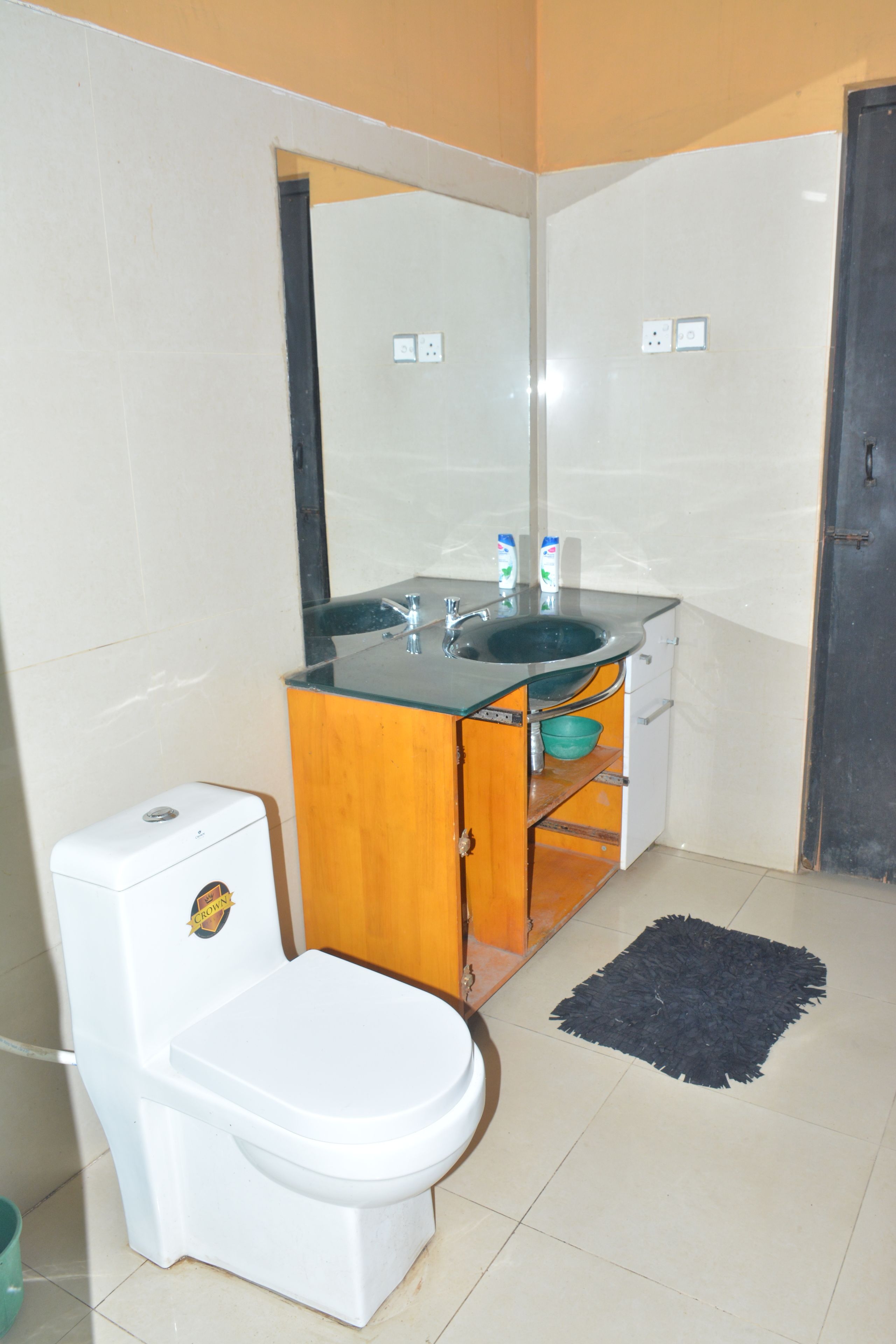 A compact bathroom with a white toilet, a wooden cabinet with a sink, and a black rug on the floor.