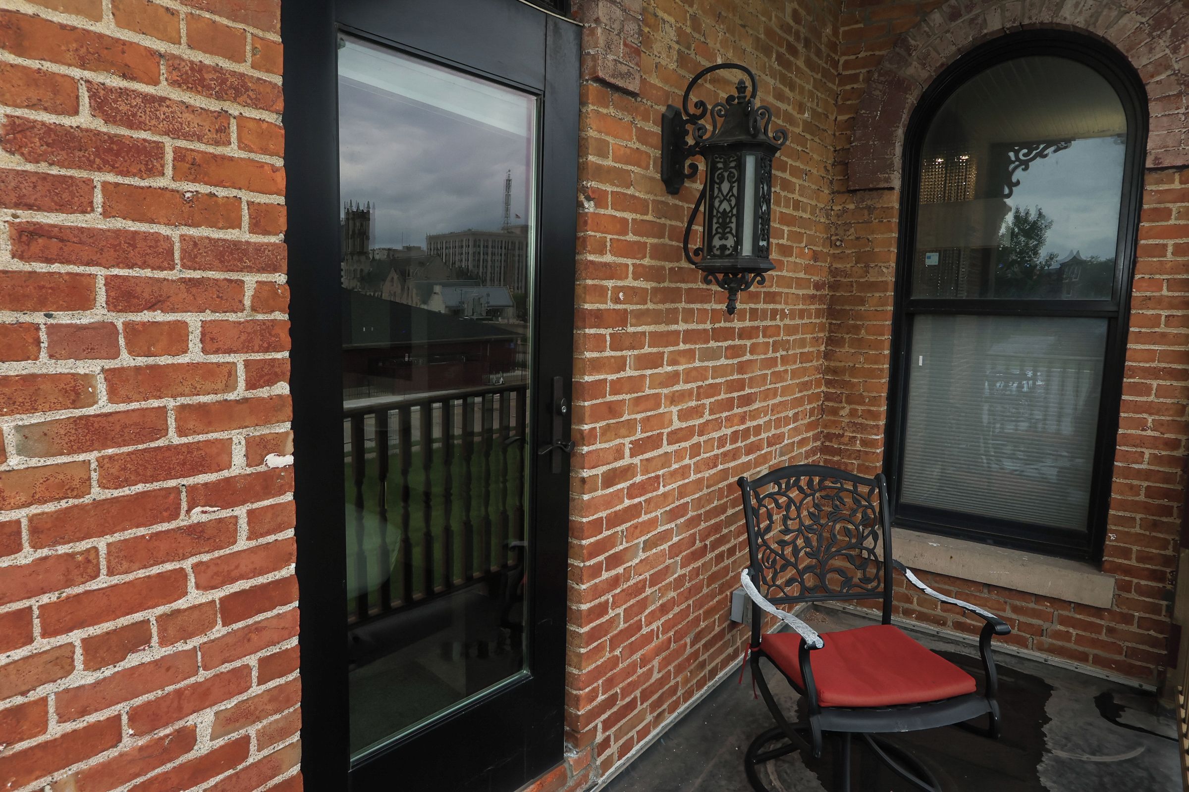 A brick building with a glass door, a metal chair with a cushion, and a decorative lantern.