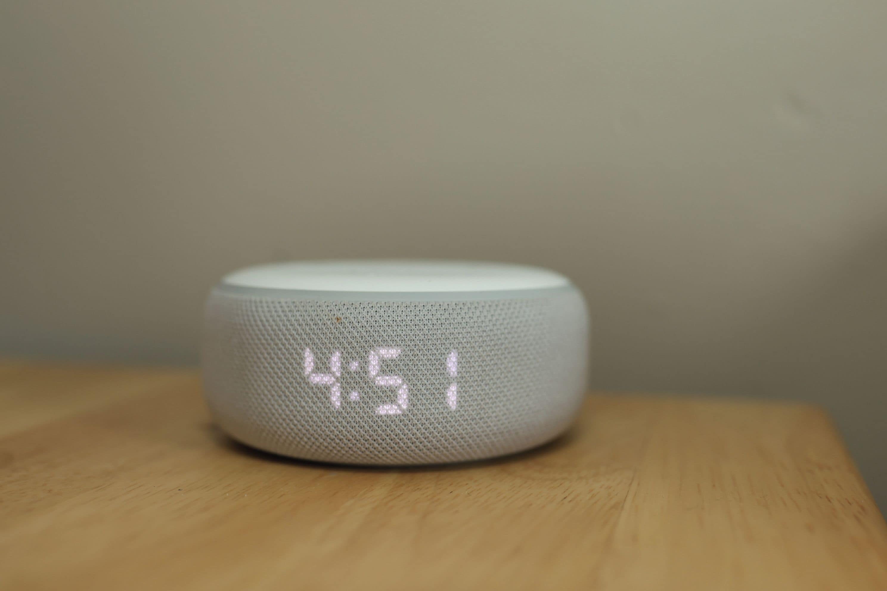 A white digital clock with a mesh design on a wooden surface.