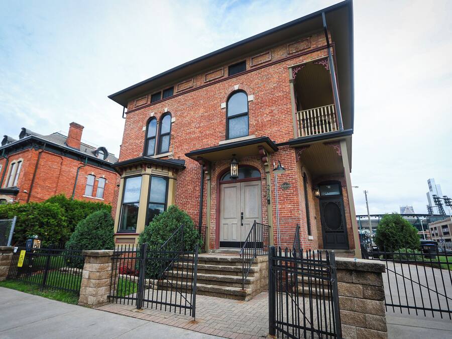 A two-story brick building with a front entrance, a balcony on the second floor, and a stone fence in front.