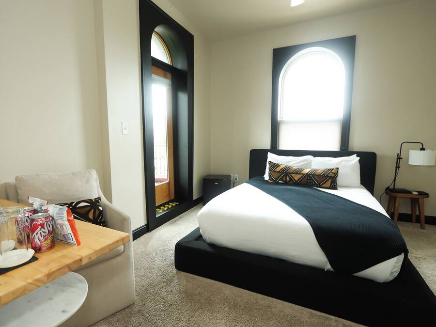 A hotel room with a bed, a desk with a chair, a lamp, and a window.