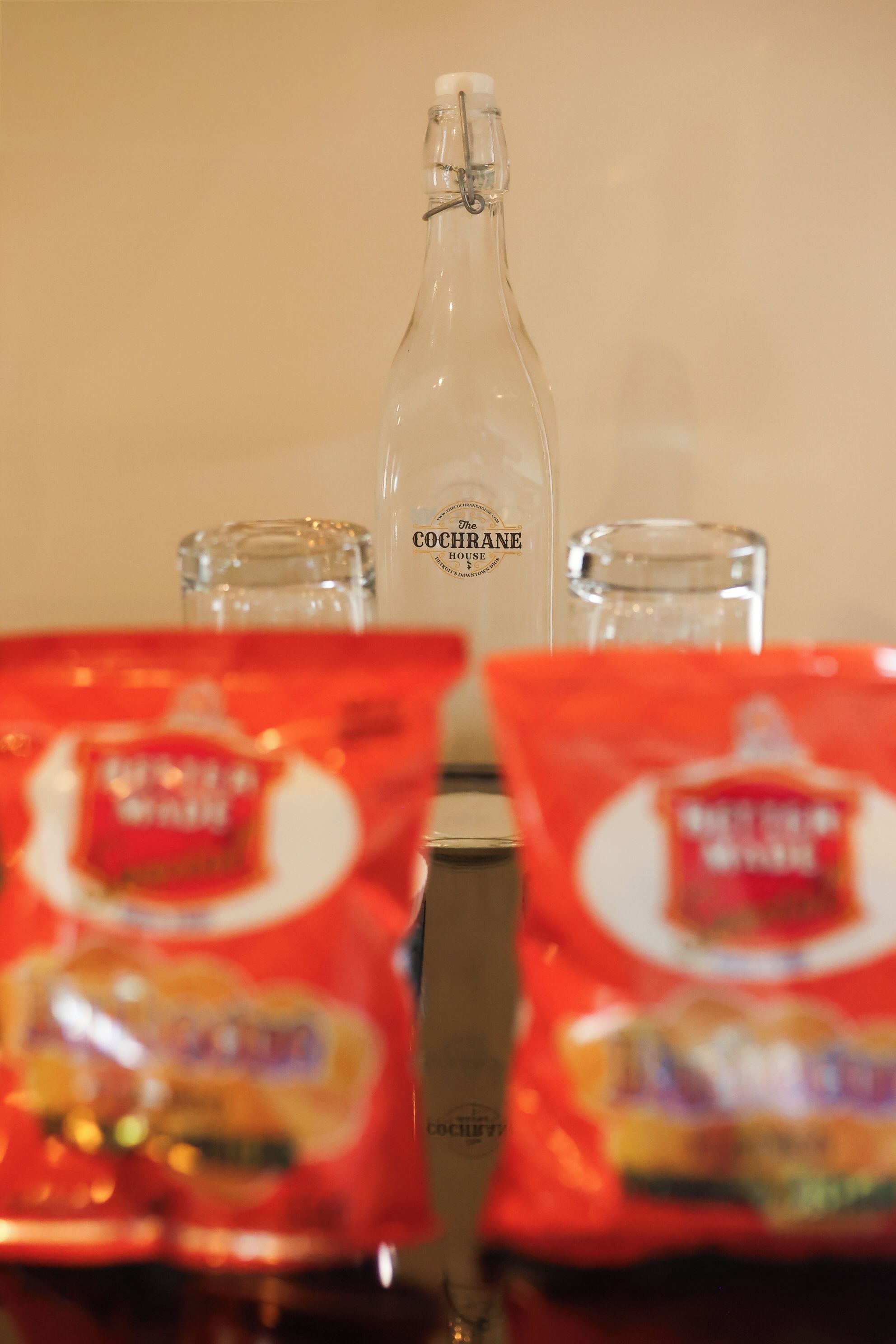 A bottle of COCHRANE, two glasses, and two packets of snacks on a table.