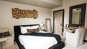 A hotel room with a large bed, a chair, a desk, a mirror, and a wall art piece.