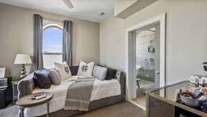 Une chambre d’hôtel moderne équipée d’un lit, d’un bureau, d’une chaise, d’une petite table et d’une salle de bain visible à travers une porte en verre.