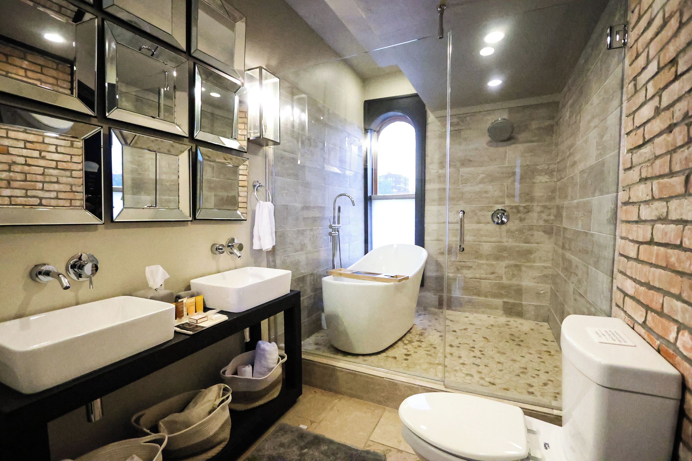 A modern bathroom with a large mirror, two sinks, a toilet, and a shower area.
