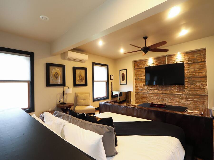 A modern living room with a sofa, a flat-screen TV mounted on a brick wall, and a ceiling fan.