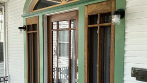 Una casa tradizionale con facciata verde e bianca, una porta in legno con vetri e un piccolo portico.