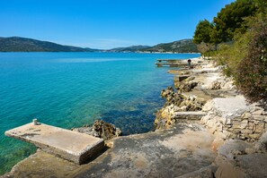 A coastal scene with clear blue water, rocky shore, and a pier extending into the sea. - Semi detached house in nature for family vacations (Seget Vranjica)