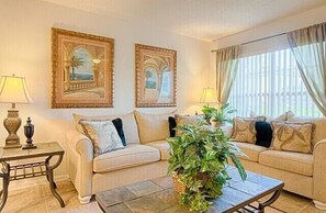 Relax in this stylish living room with a sofa, armchairs, and a coffee table, surrounded by artwork and a large potted plant.