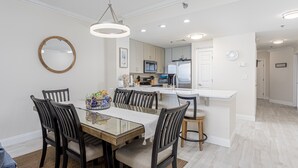 Une cuisine moderne avec des meubles blancs, un îlot central et un coin repas comprenant une table en verre et des chaises foncées.