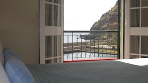 Un dormitorio con cama, almohadas y vistas a un balcón con barandilla y un colgador de luz.